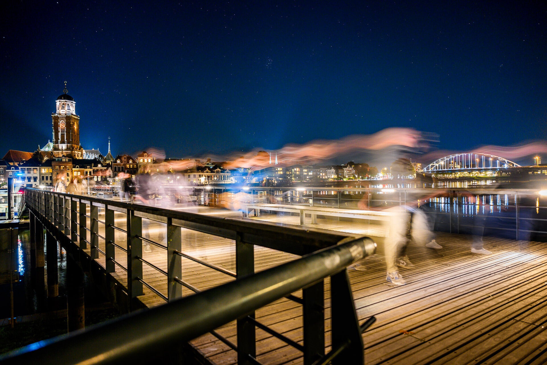 Het Wellepad over de IJssel bij nacht, met de verlichte Lebuinustoren en de Wilhelminabrug in Deventer, foto door Raymond Rothengatter